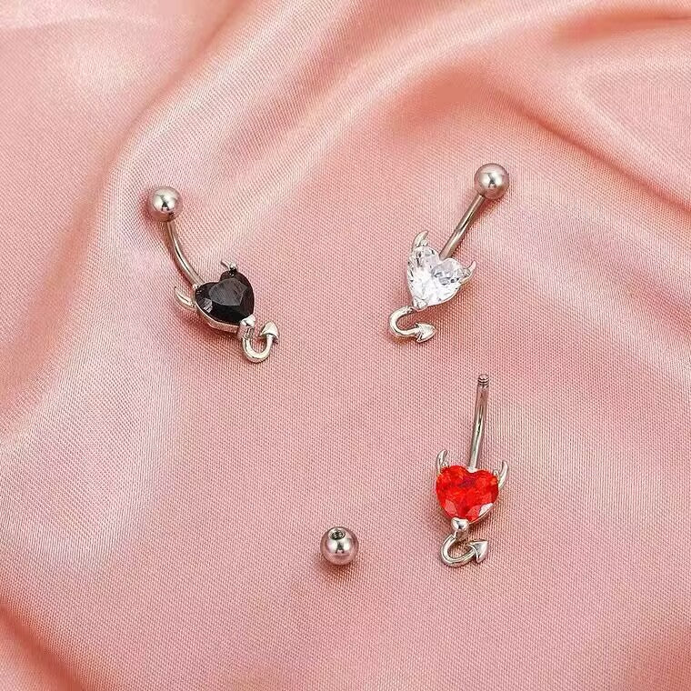 An externally threaded 14G curved barbell navel piercing ring showing a detached 5mm top ball on pink satin fabric.
