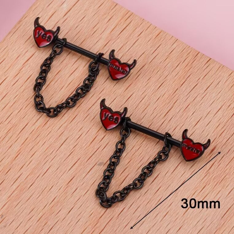 Close-up photo of devil heart nipple jewelry on a wooden background showing a 30mm length measurement.