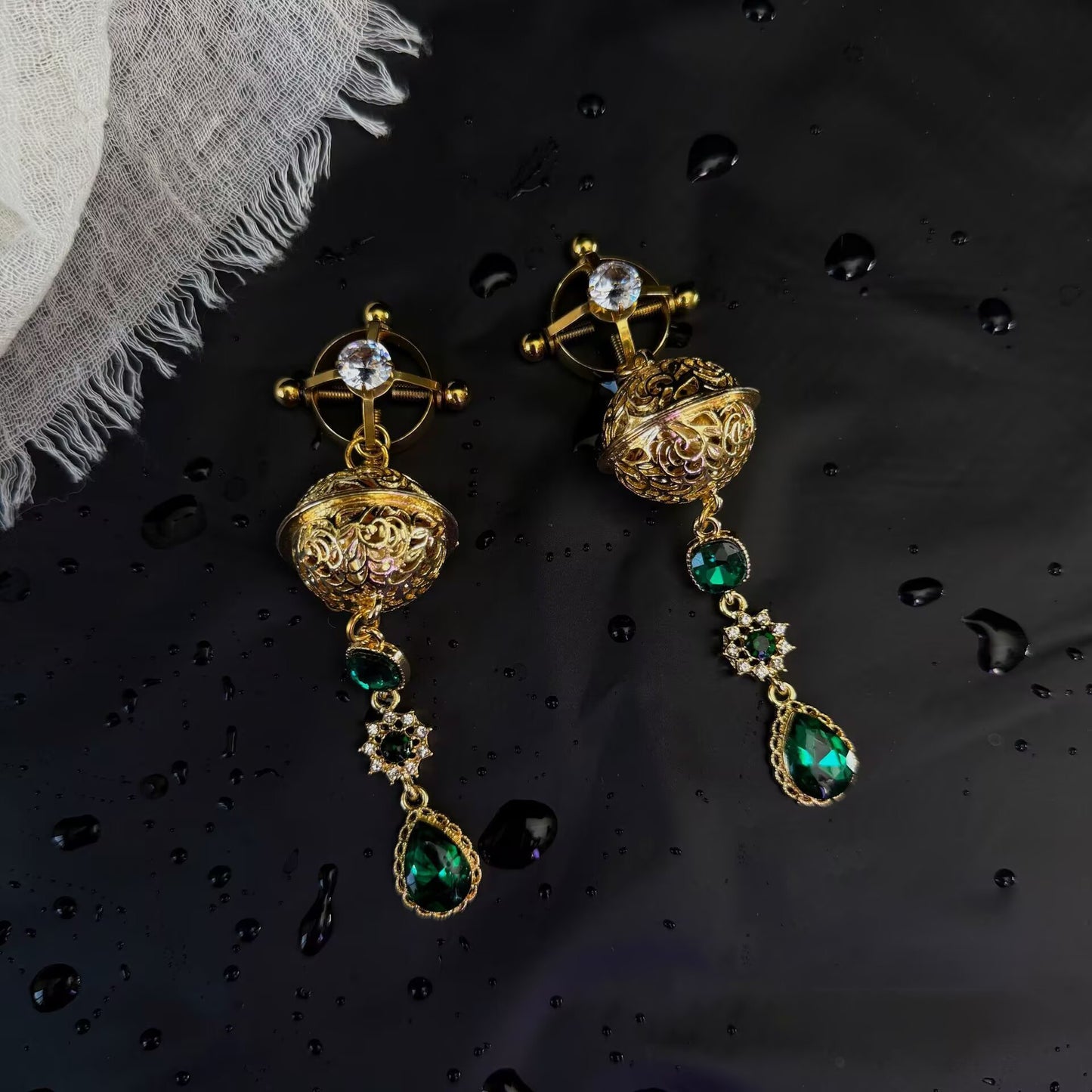 Gold 4-screw adjustable shield ring non-pierced nipple clamps decorated with crystal studs and emerald green dangle charms.