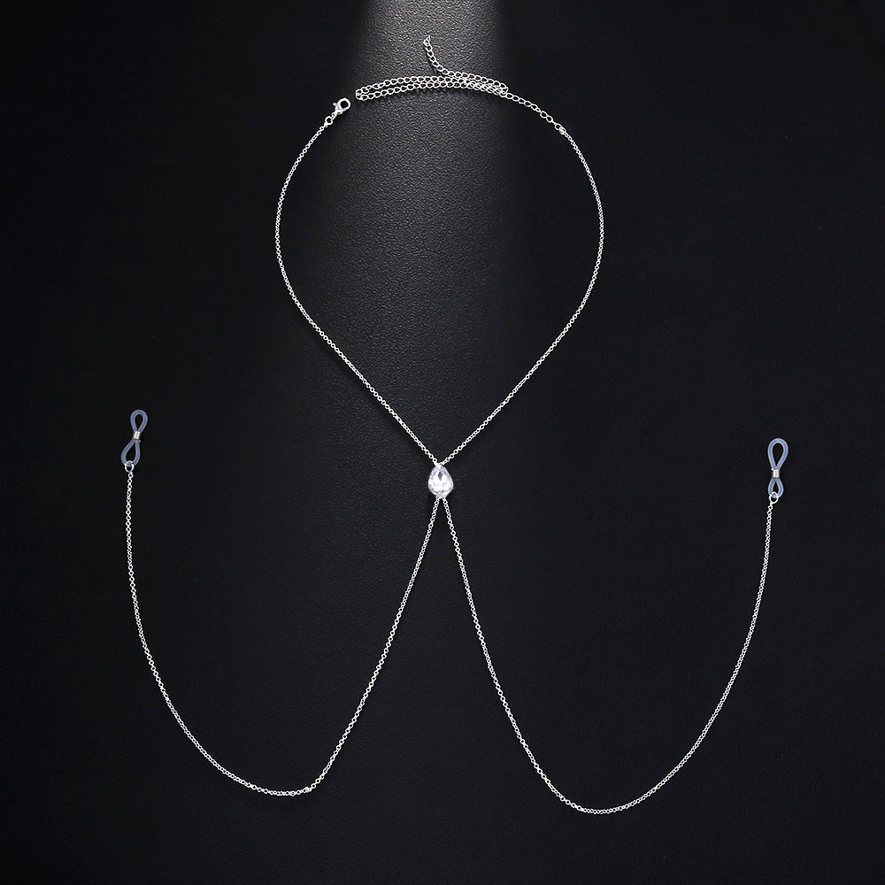 Flat lay product view of an adjustable fake nipple piercing body chain jewelry with a clear white teardrop rhinestone and soft silicone loops on a black background.