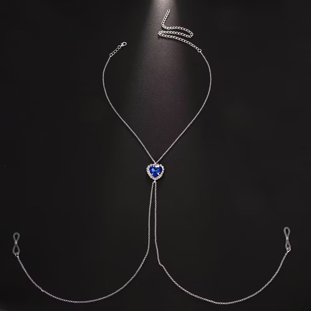 A silver body chain with a vibrant blue rhinestones heart centerpiece connected to adjustable rubber loop ends for a non-piercing faux nipple ring look.