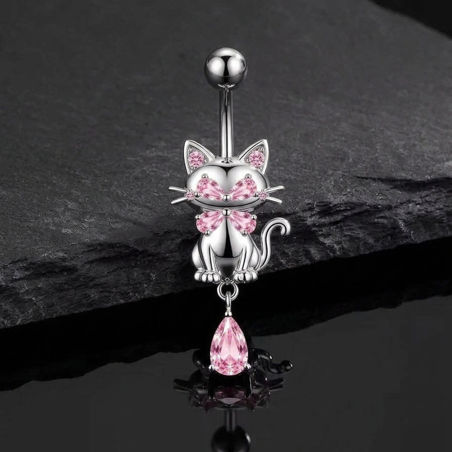 Pink crystal cat dangle navel piercing jewelry displayed on a dark slate stone background, highlighting the sparkling details.
