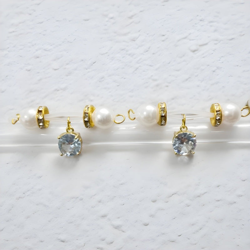 Matching pair of gold-tone non-piercing nipple jewelry with white pearl-look ends and round clear charms on a display bar