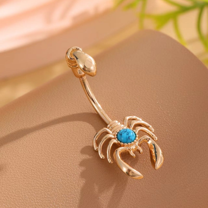 Single gold-tone scorpion belly button ring with sculpted claws and a blue veined center on tan.