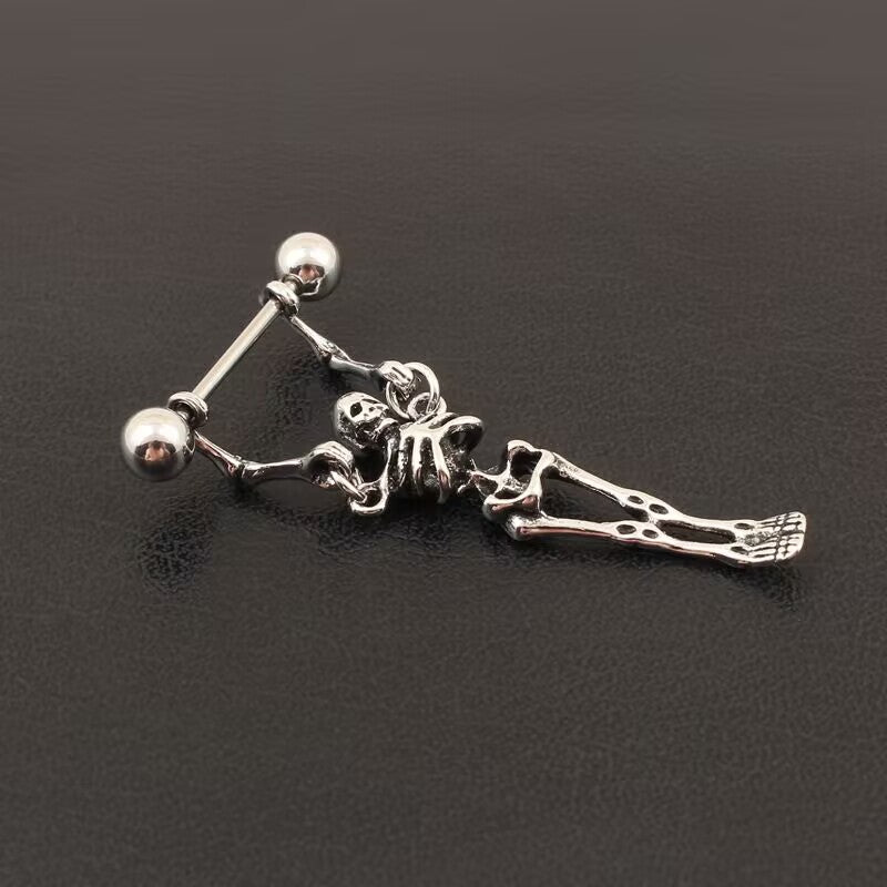Flat lay view of gothic alternative style skeleton dangle nipple ring set on dark textured background.