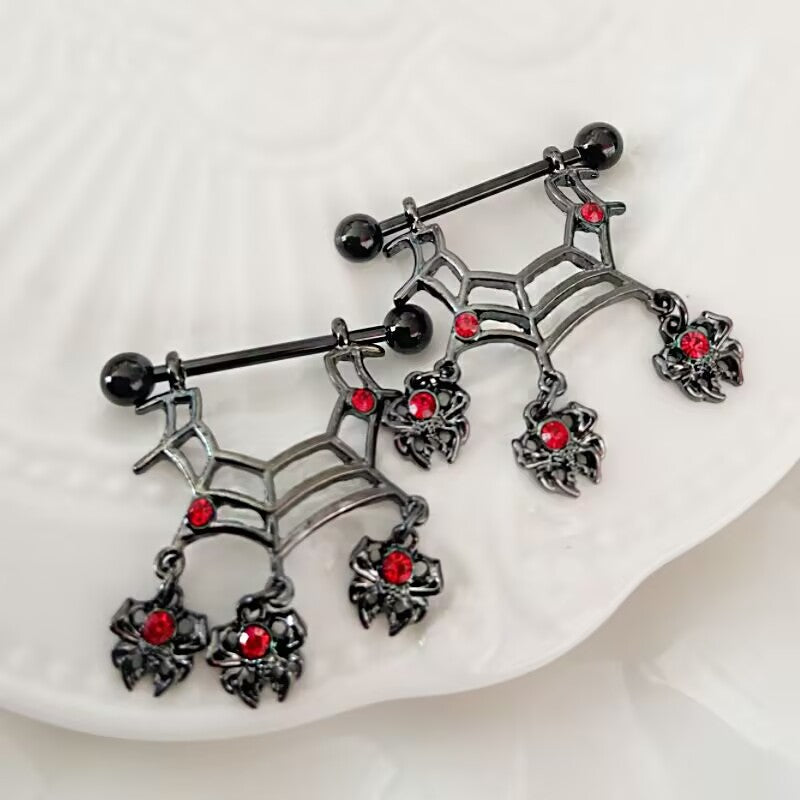 Two black spider web nipple shields with red gems laid out on a decorative dish for gothic body jewelry display.