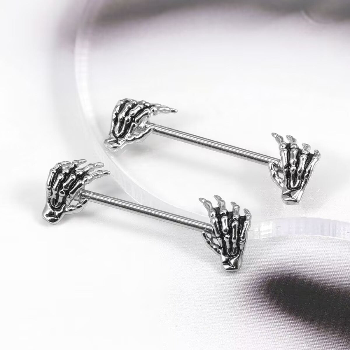 Close-up lifestyle shot of two skeleton hand nipple bars on a reflective surface.