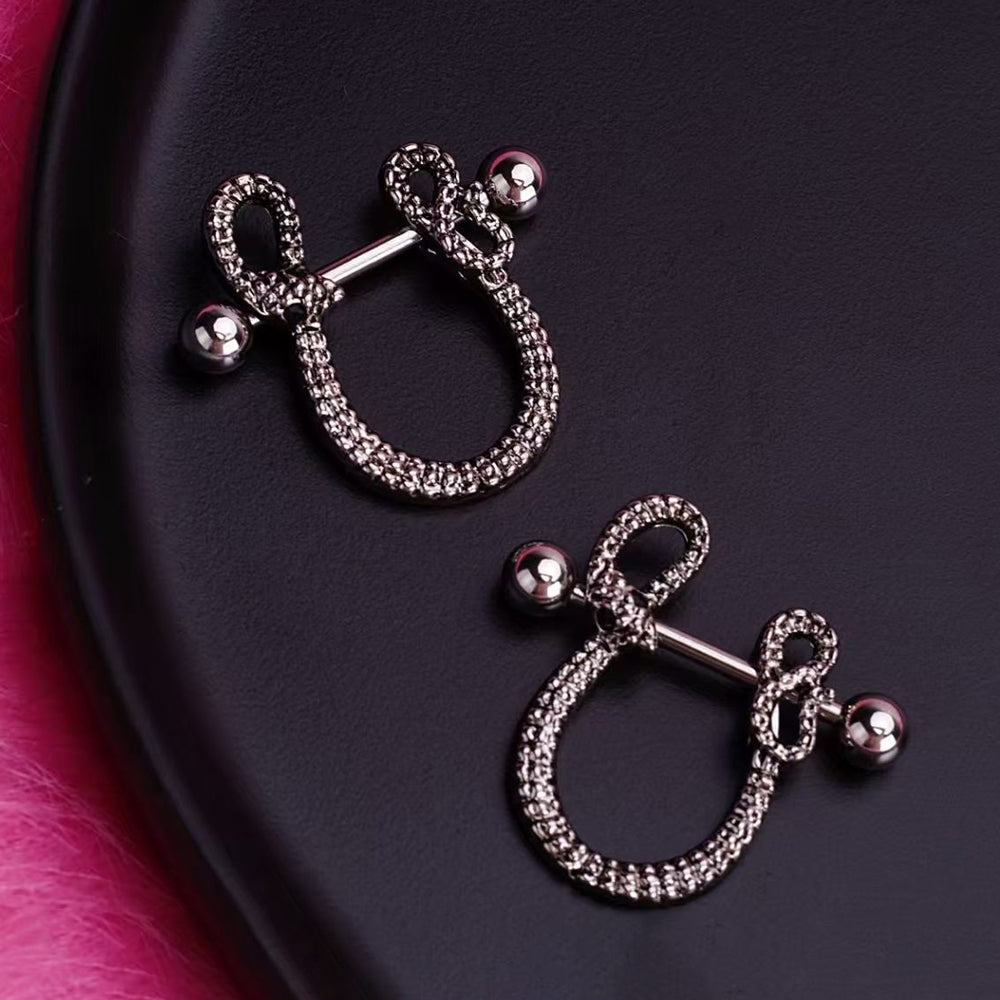 A pair of Gothic snake-style nipple rings with dark silver finish displayed on a sleek black surface.