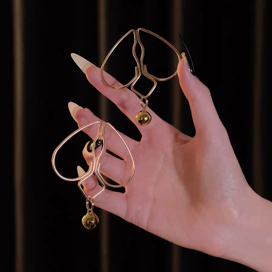 A person holding a pair of gold heart-shaped body clamps with jingle bells.