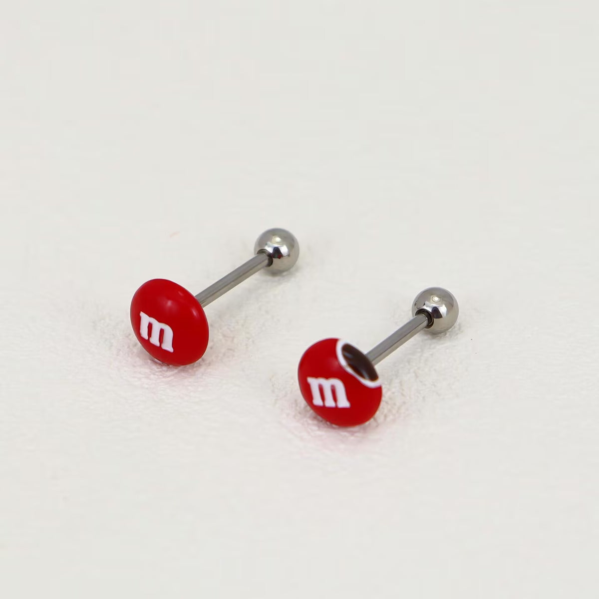 Pair of vibrant red M&M candy tongue barbells with glossy finish and threaded back balls.