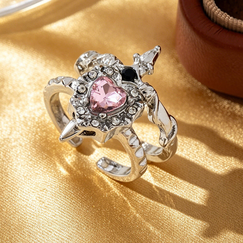 Silver-tone pink heart and black-accent sword open rings overlapping on gold fabric