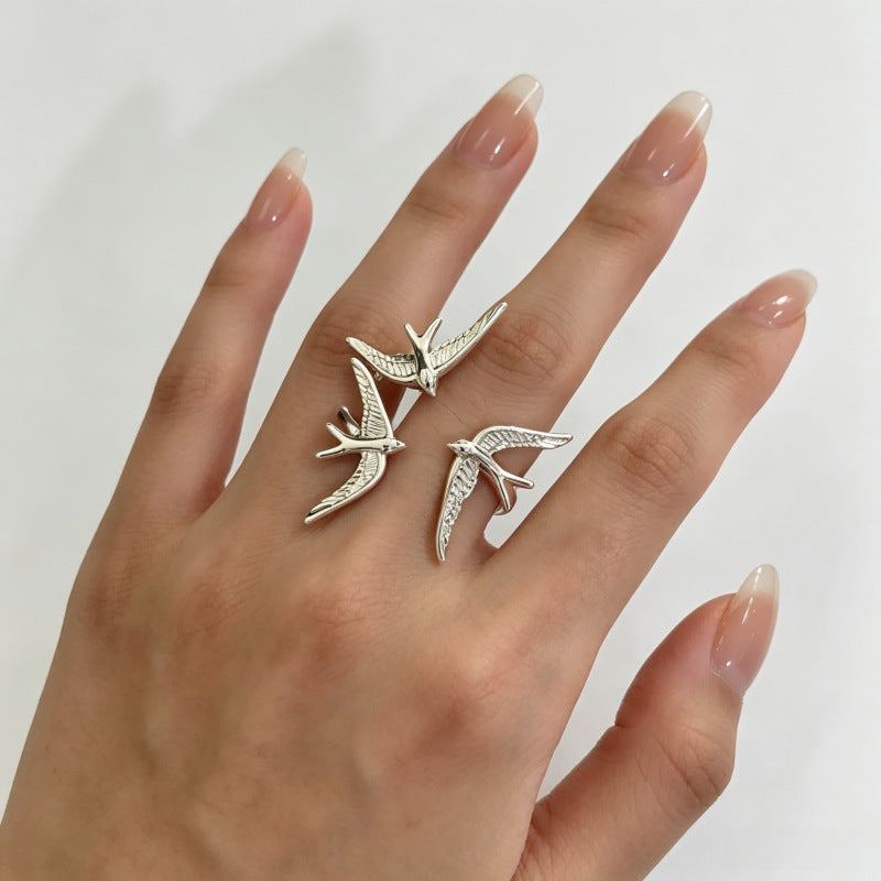 One silver-tone three-swallow statement ring worn on a hand with fingers spread.