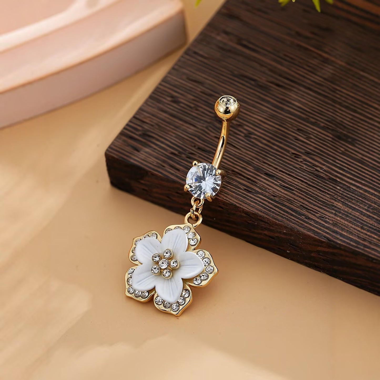 Side view of a sparkling crystal floral belly ring resting on a wooden surface, showcasing the flower detail.