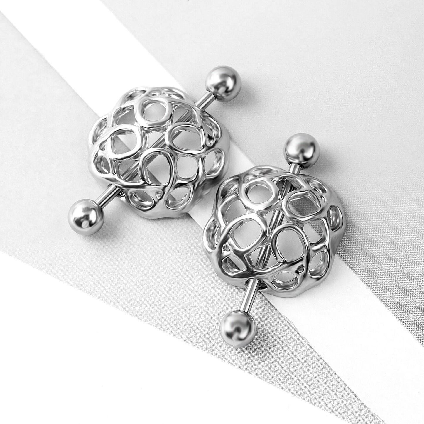 Aesthetic lifestyle view of two intricate cage design nipple rings on a white background.