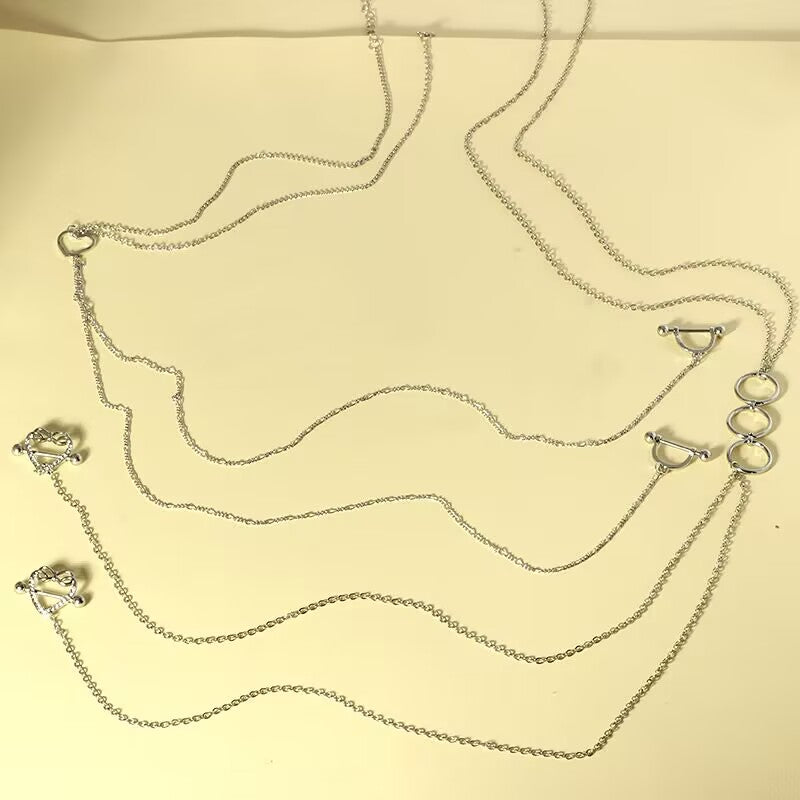 A side-by-side arrangement of both the triple O-ring style and the hollow heart style silver nipple piercing body chains on a warm cream background.