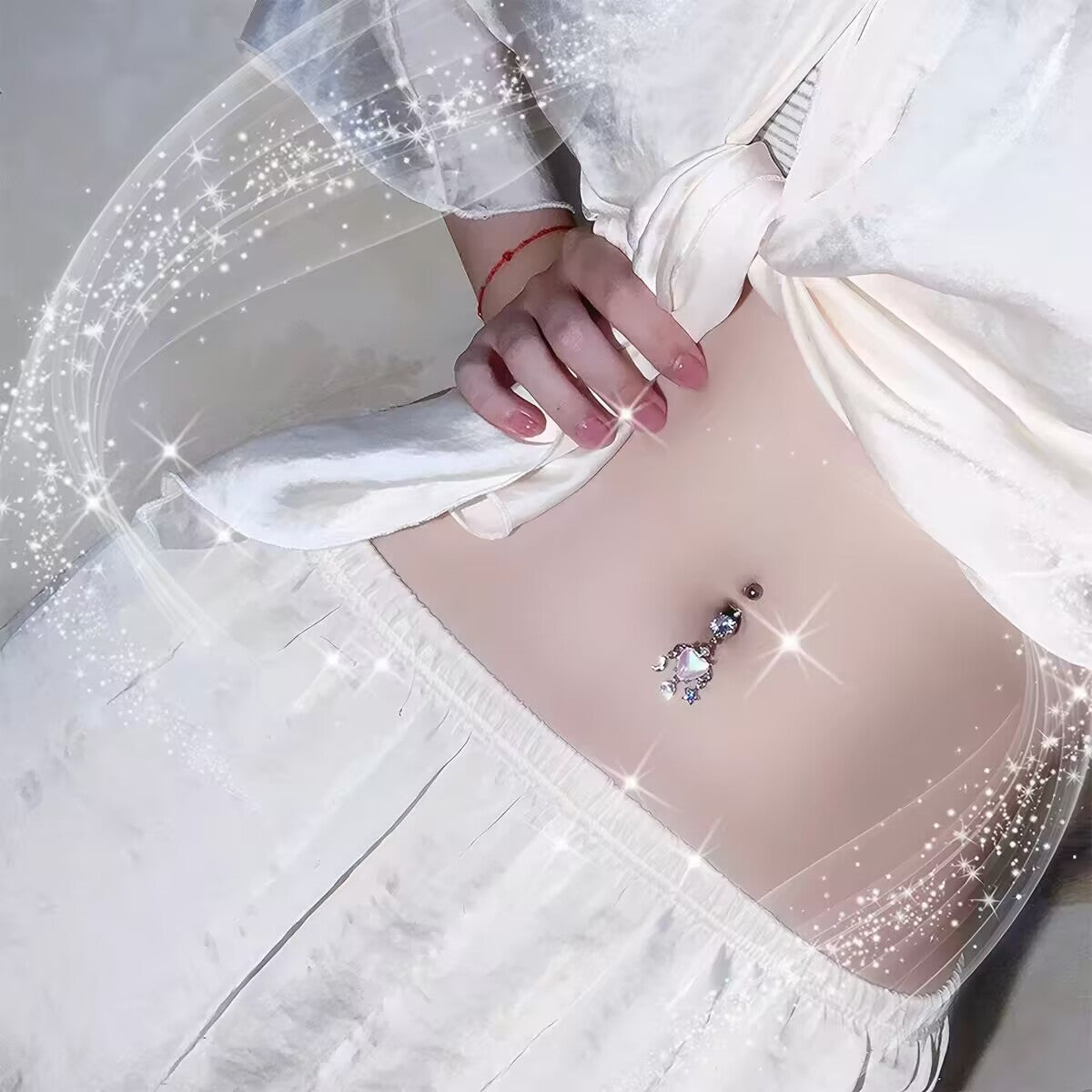 Model wearing a shiny fairycore heart navel ring with crystal moon and star dangles.
