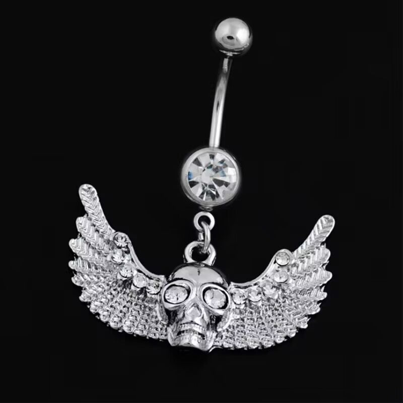 Close-up shot of the Y2K punk style dangling winged skull belly ring with rhinestone eyes on a dark background.