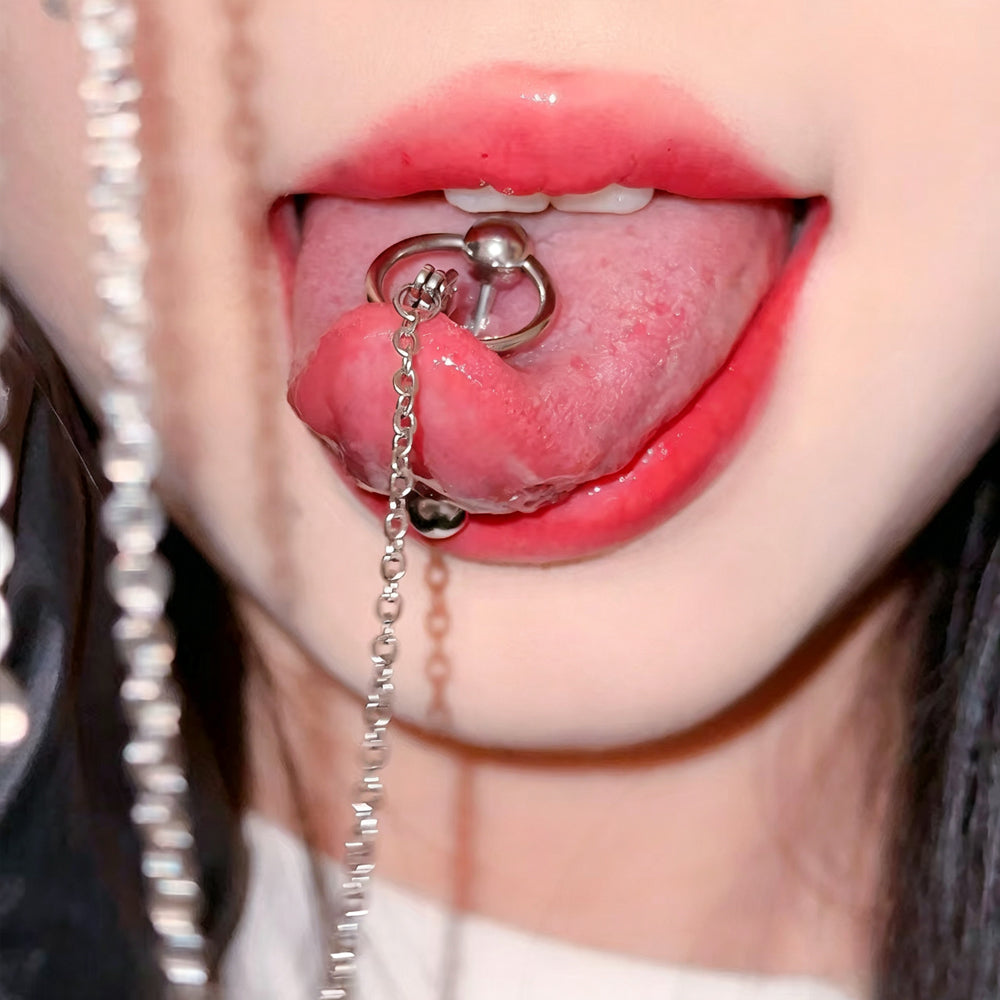 Close-up of a person showing a stainless steel tongue piercing barbell connected to a long, delicate metal chain on a pink tongue.