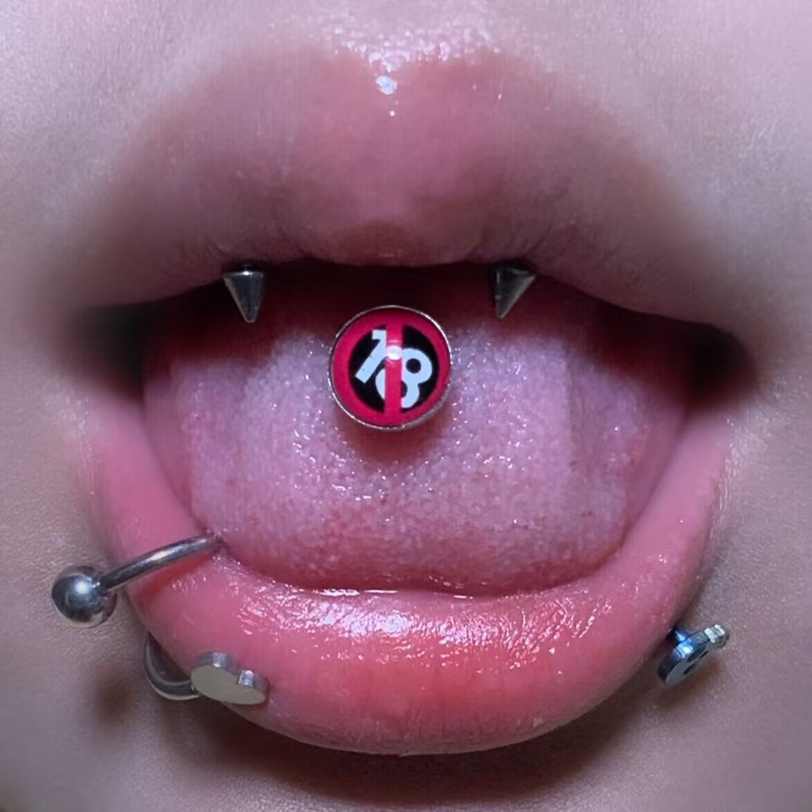 Close-up of 18 restricted symbol tongue barbell piercing styled with lip piercings.