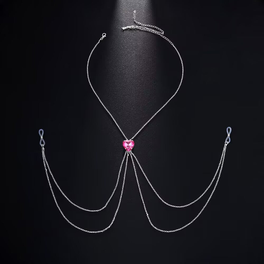 Flat lay view of an adjustable fake nipple piercing body chain featuring a romantic pink heart crystal centerpiece and multi-layer silver chains with adjustable silicone loops on a black background.