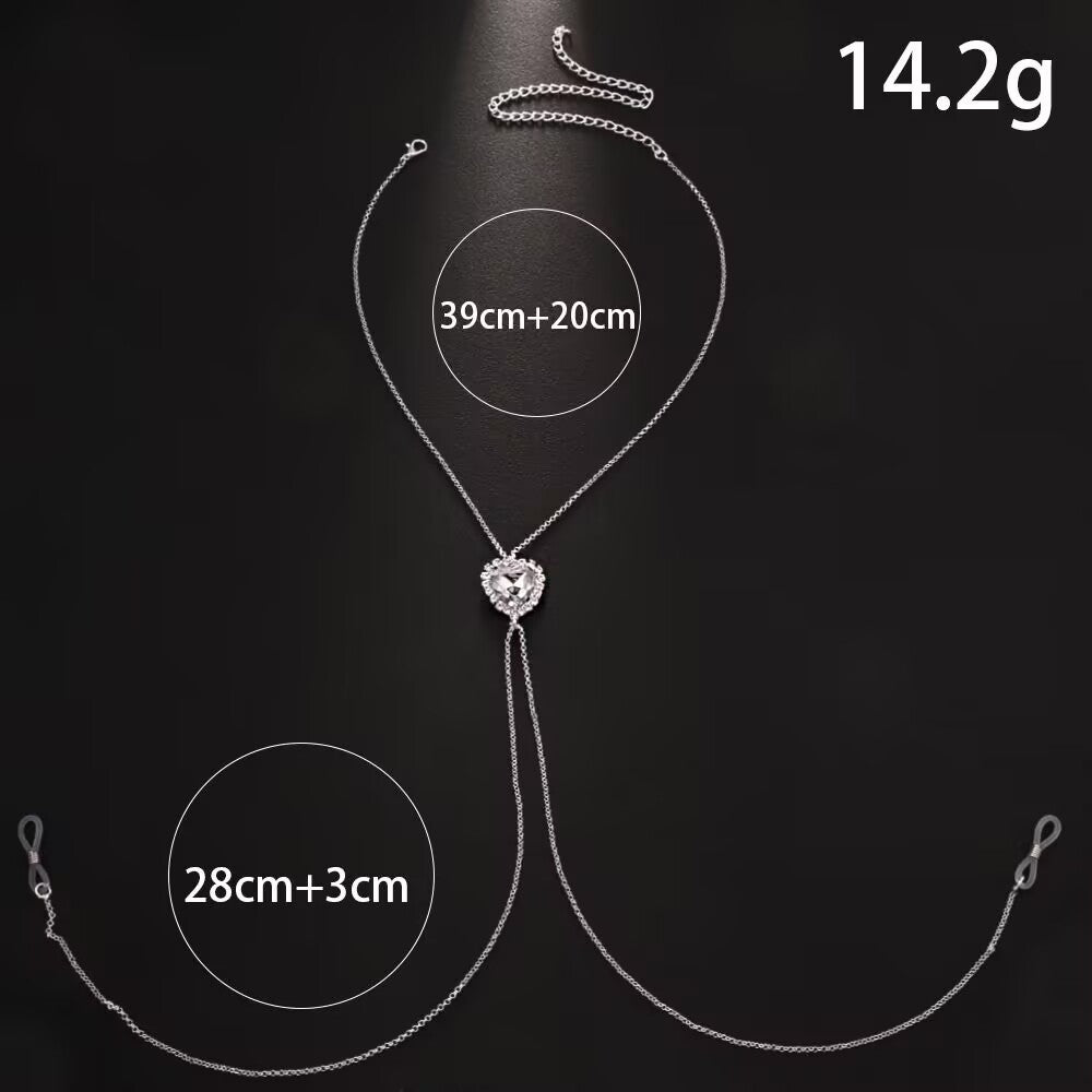 Product layout of a clear crystal heart fake nipple chain necklace on a black background, indicating a weight of 14.2g, necklace length of 39cm plus 20cm, and drape chains of 28cm plus 3cm with rubber loops.