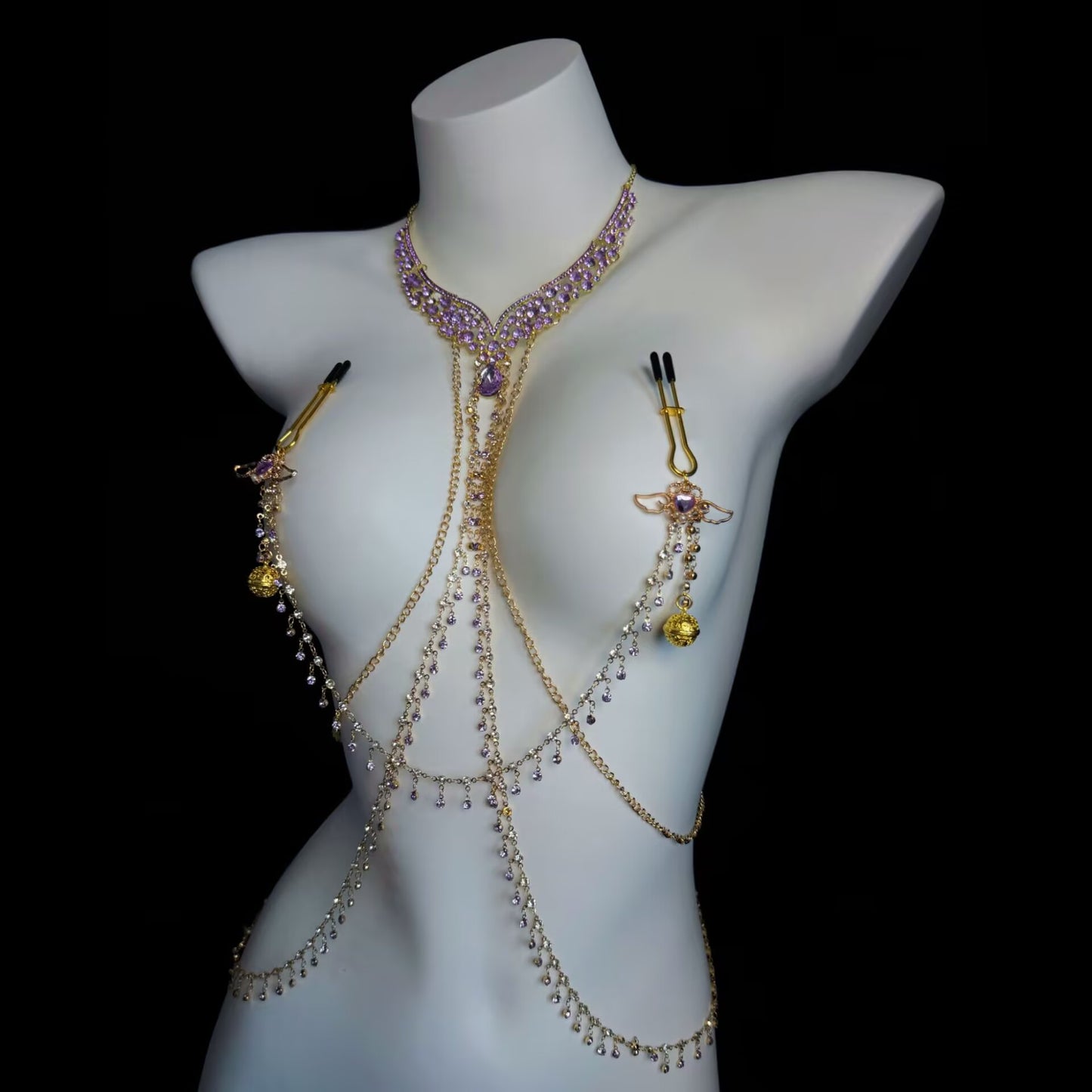 Gold body jewelry harness showcasing long adjustable pin-style nipple clamps and dangling purple jewel accents.