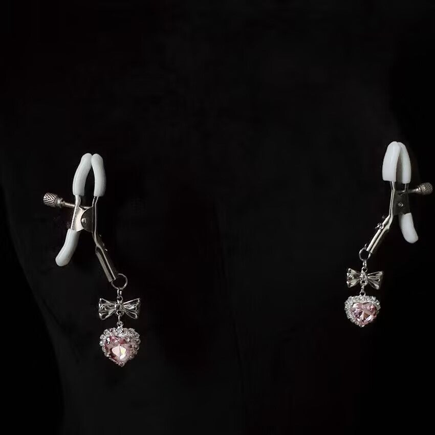 Pair of adjustable metal nipple clamps with protective white silicone tips and pink heart crystals.