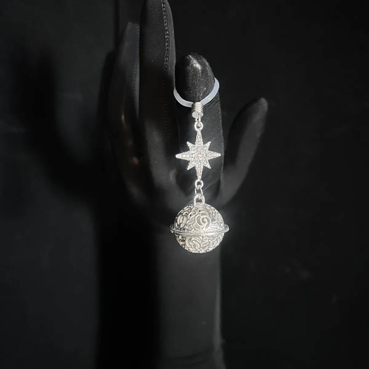 Demonstration of the adjustable silicone loop on a black gloved hand showing the North Star and orb pendant.