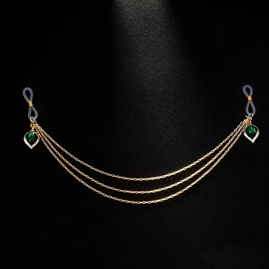 Product display of a gold connected fake nipple piercing jewelry chain featuring three-layered chains and vintage green teardrop gems on a black background.
