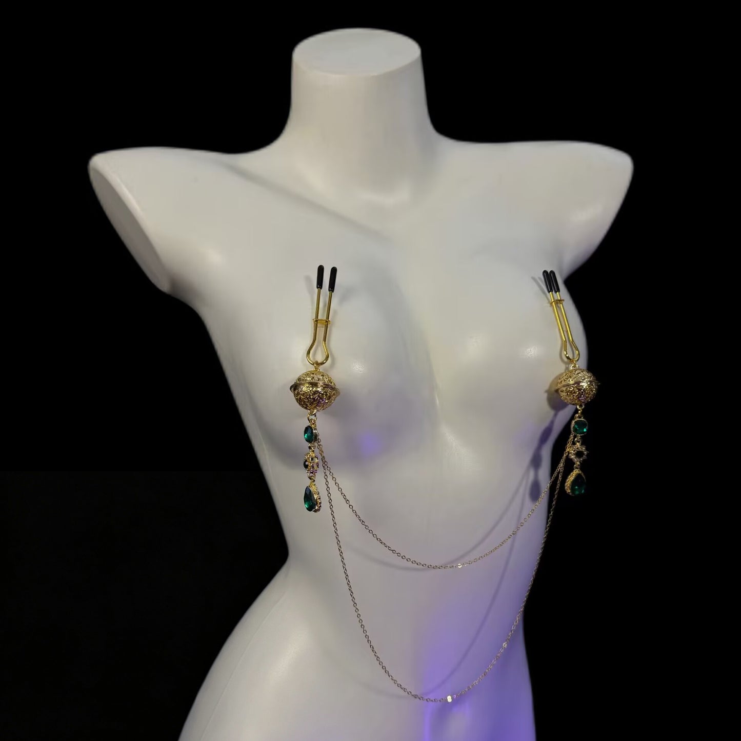 Adjustable U-shaped rod nipple clamps with gold filigree sphere and emerald teardrop pendant linked by body chains.