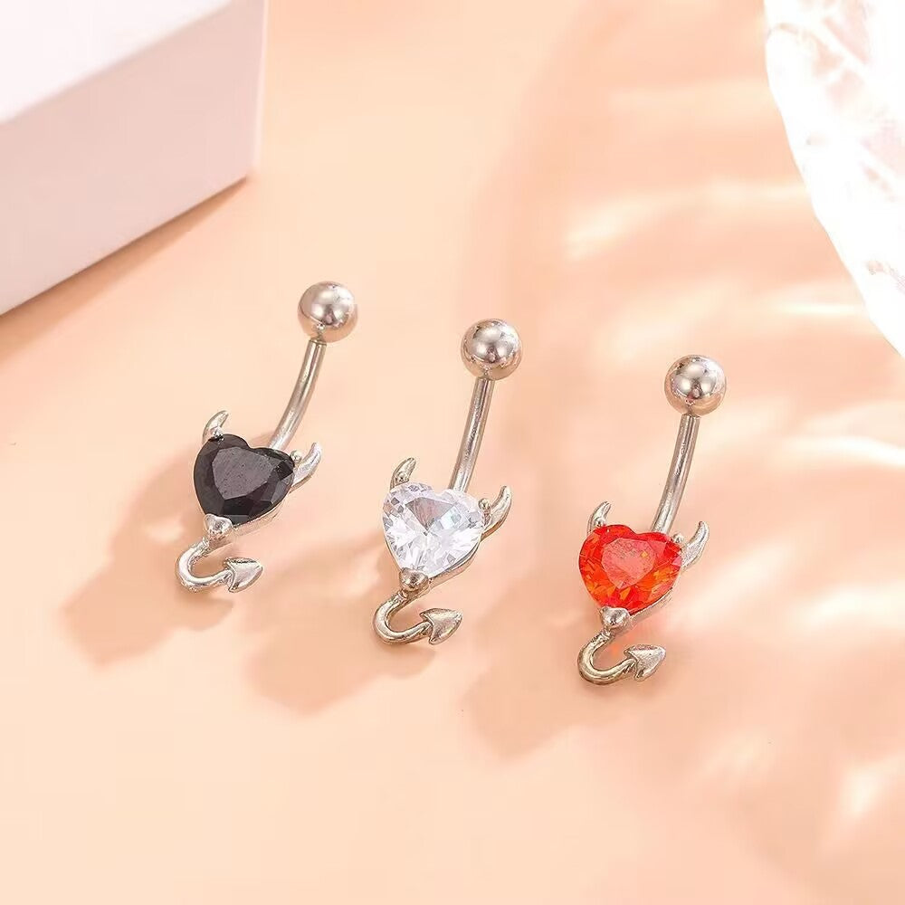 Aesthetic real-life shot of black, clear, and red crystal devil heart belly piercing rings reflecting natural sunlight.