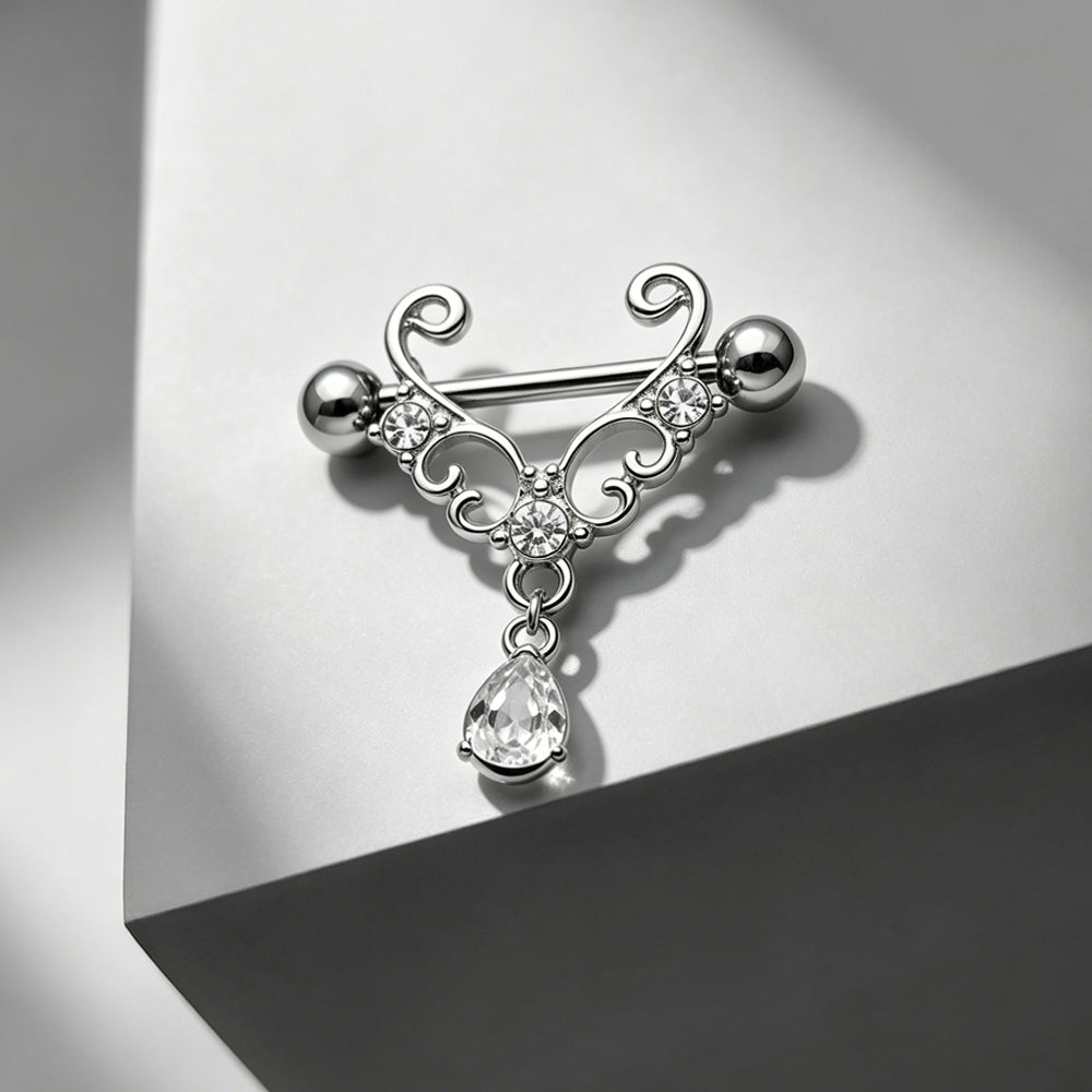An artistic aesthetic shot of a silver gothic dangle nipple shield resting on a modern geometric block with elegant, soft studio lighting and shadows.