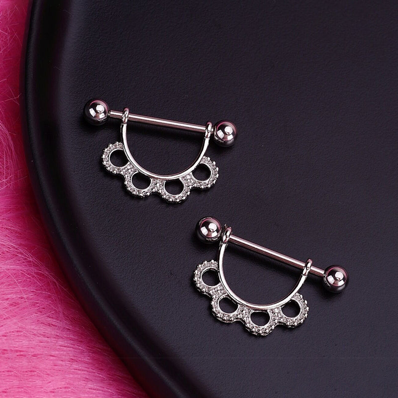 A pair of elegant scalloped nipple barbells displayed on a sleek black surface, highlighting the intricate craftsmanship and sparkling details.
