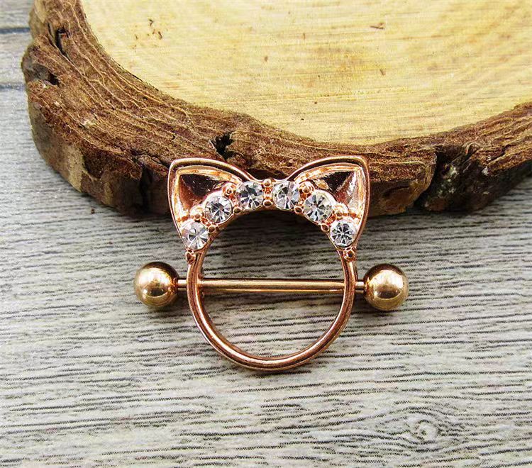 Close-up real life shot of a rose gold cat shield nipple ring with cubic zirconia on a rustic wooden background