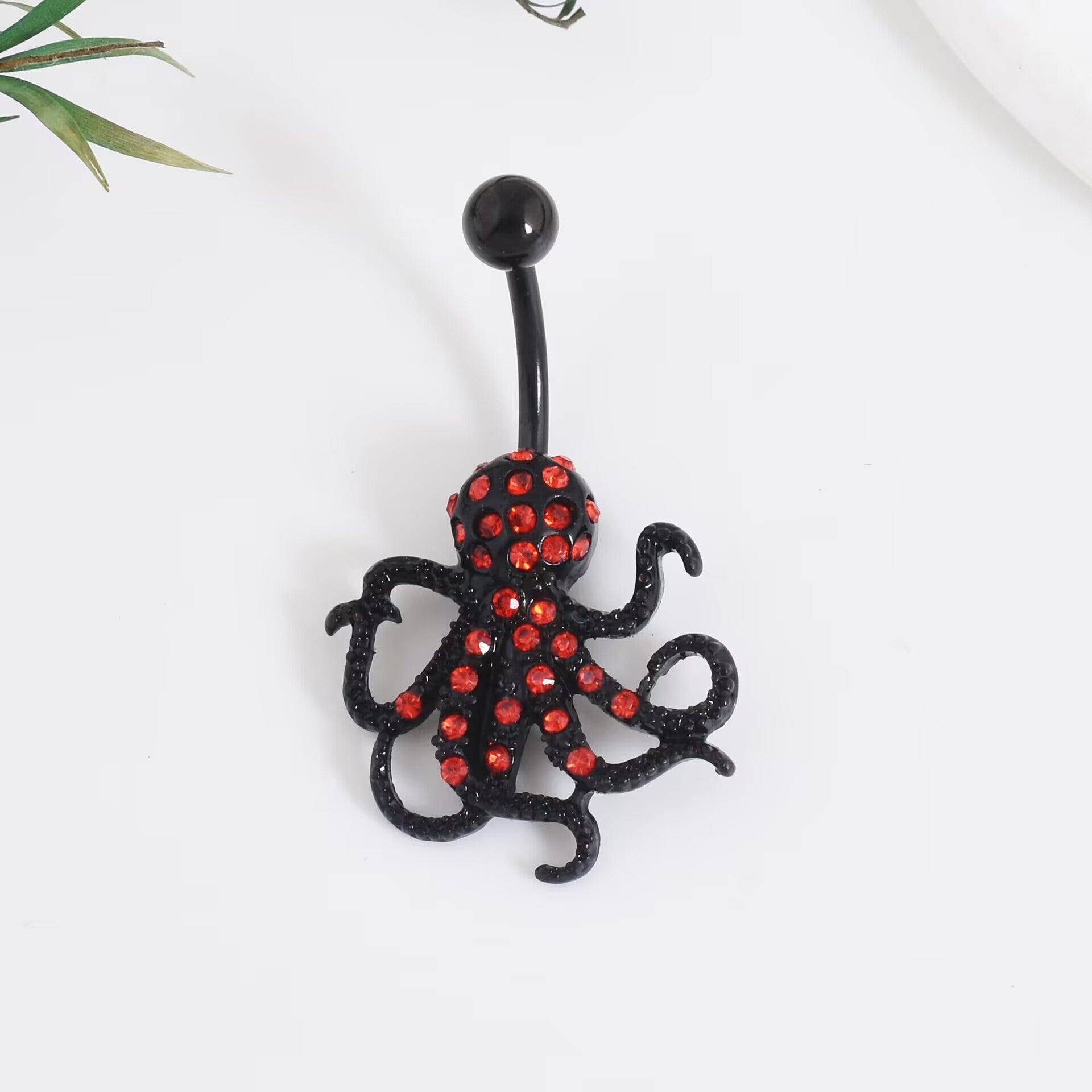 Alternative fashion black octopus pendant belly piercing with sparkling crimson red crystals, close-up view.