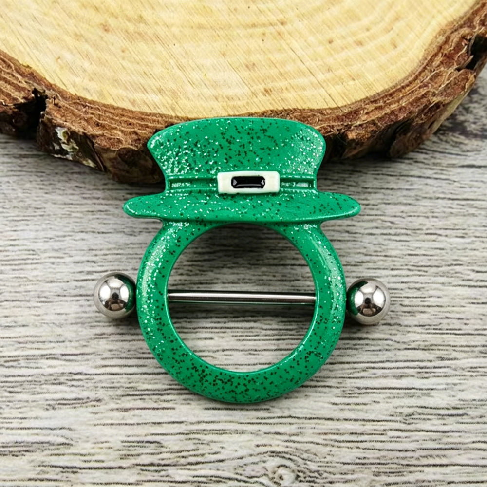 Close-up shot of a green glitter leprechaun top hat nipple shield laying flat on a rustic wood slice background, highlighting alternative festive style.