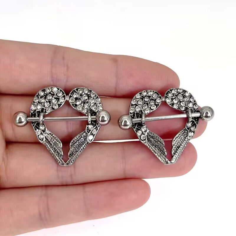 A pair of sparkling heart-shaped angel wings nipple shields held in hand for scale.
