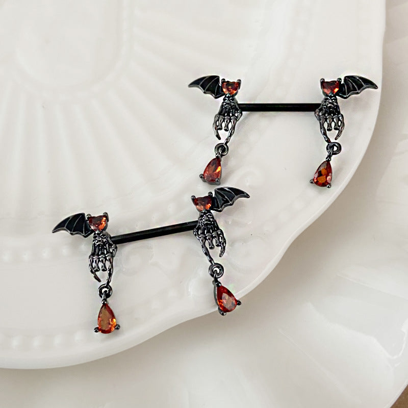 Pair of bat wing nipple barbells with skeletal hands and dangling red drops on a white dish.
