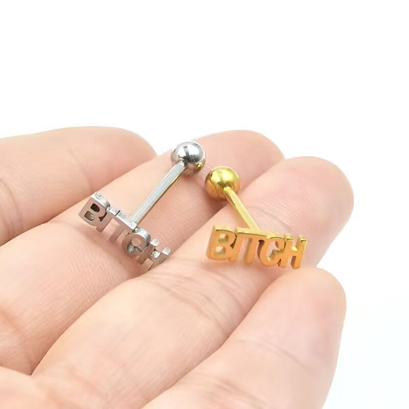 Close-up of silver and gold BITCH tongue piercing jewelry held in hand for scale.