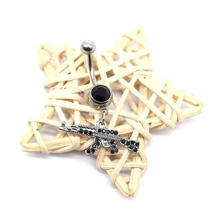 Gothic jet black cz crystal paved AK47 assault rifle dangle belly ring placed on a woven star background.