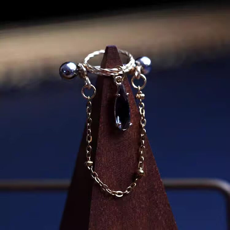 Dark purple black teardrop CZ nipple shield barbell ring with gold halo frame and accent chain.