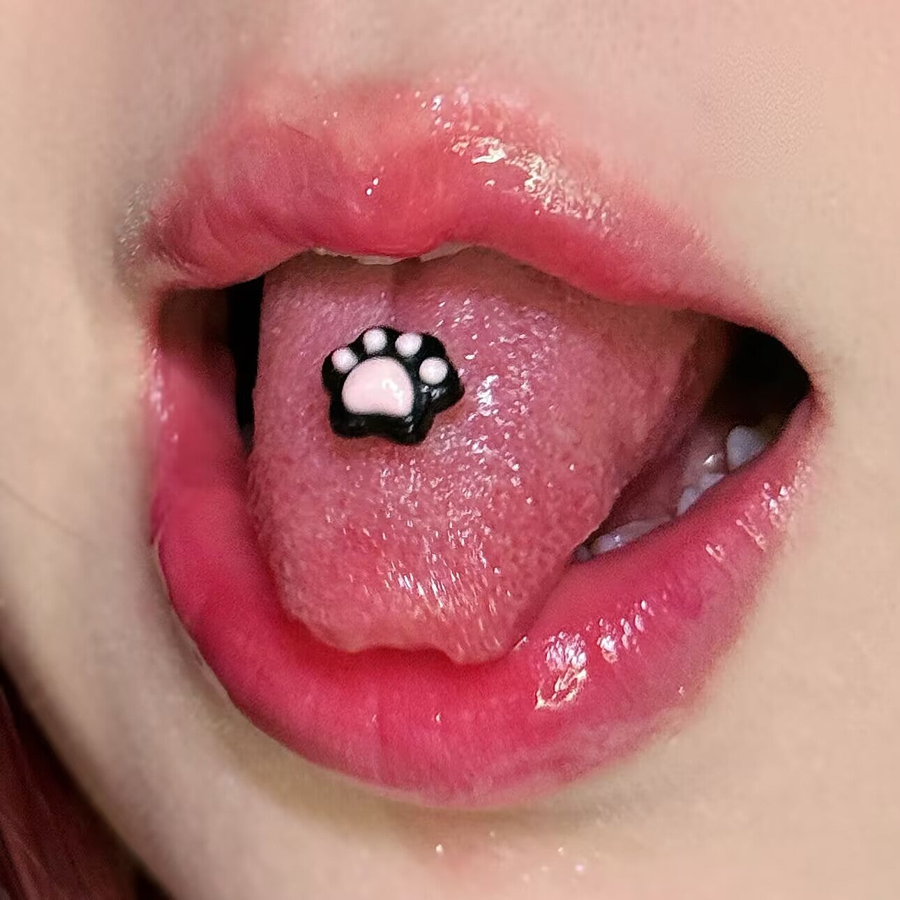 Cute black resin cat paw tongue barbell with soft pink pads placed on a tongue, edgy alt body jewelry