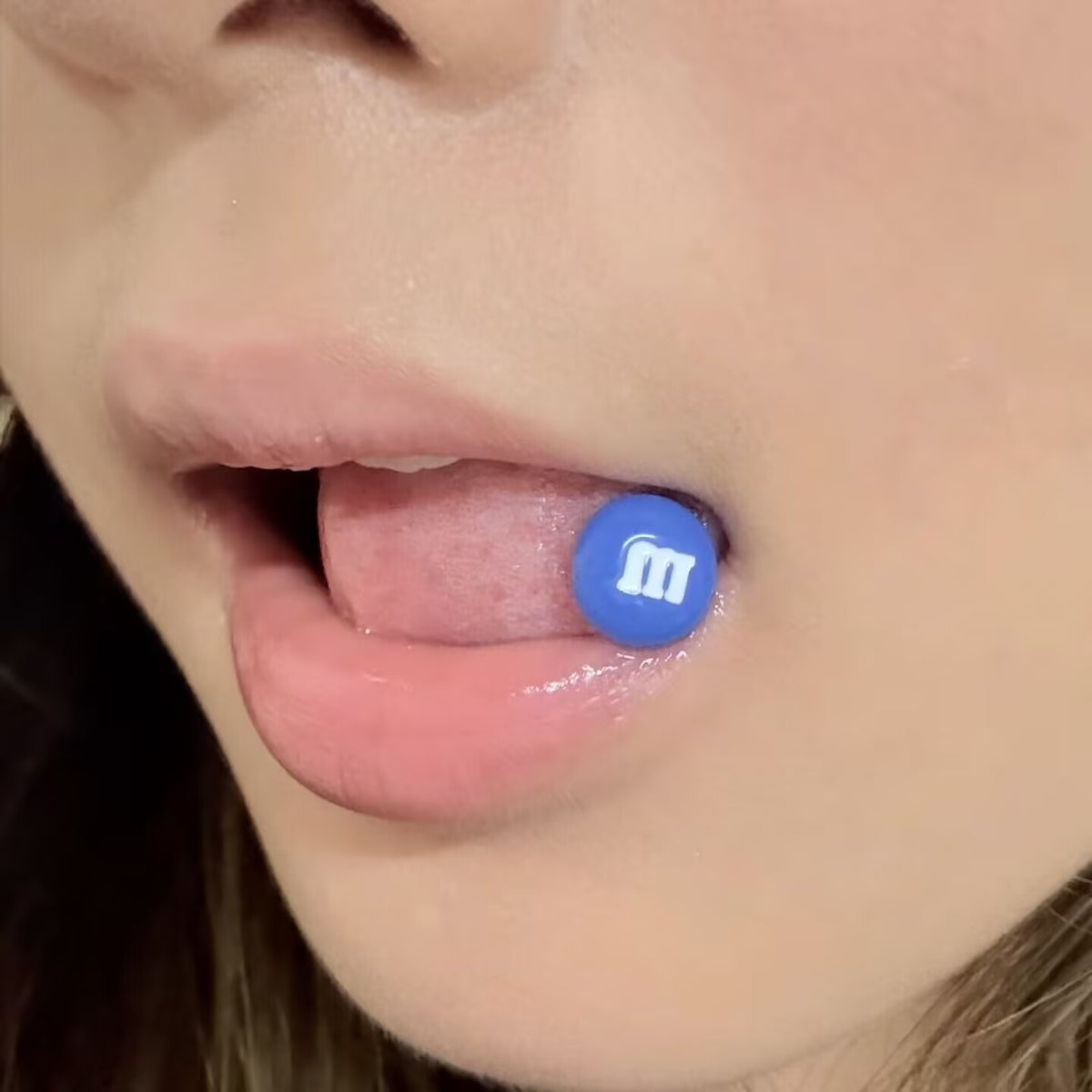 Close-up of a model wearing a bright blue M&M's candy top tongue ring piercing.