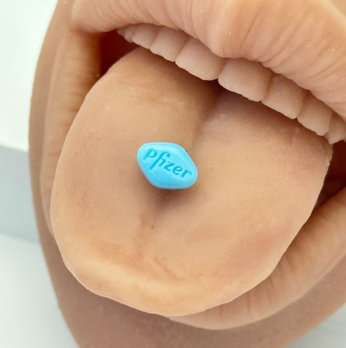 Blue pill tongue ring piercing modeled on tongue showing Pfizer text side.