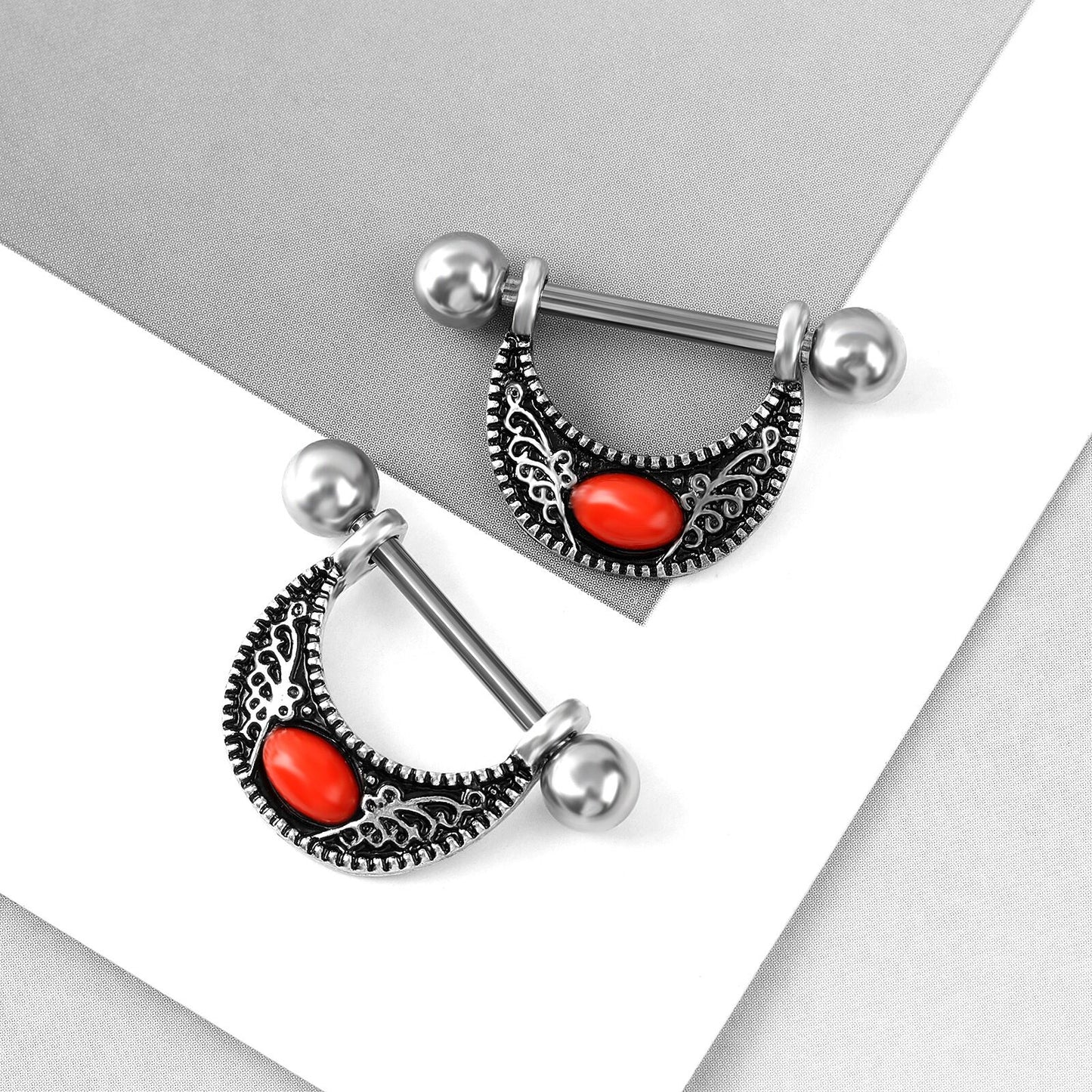 High-angle view of two vintage bohemian nipple shields with red gemstones on a clean aesthetic background.