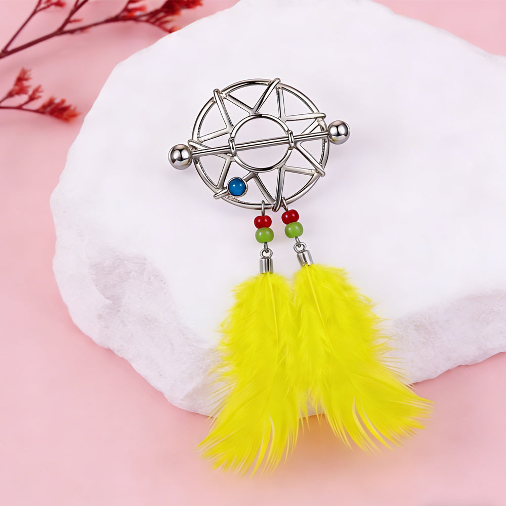 Decorative nipple jewelry with yellow feathers displayed on a white stone background.