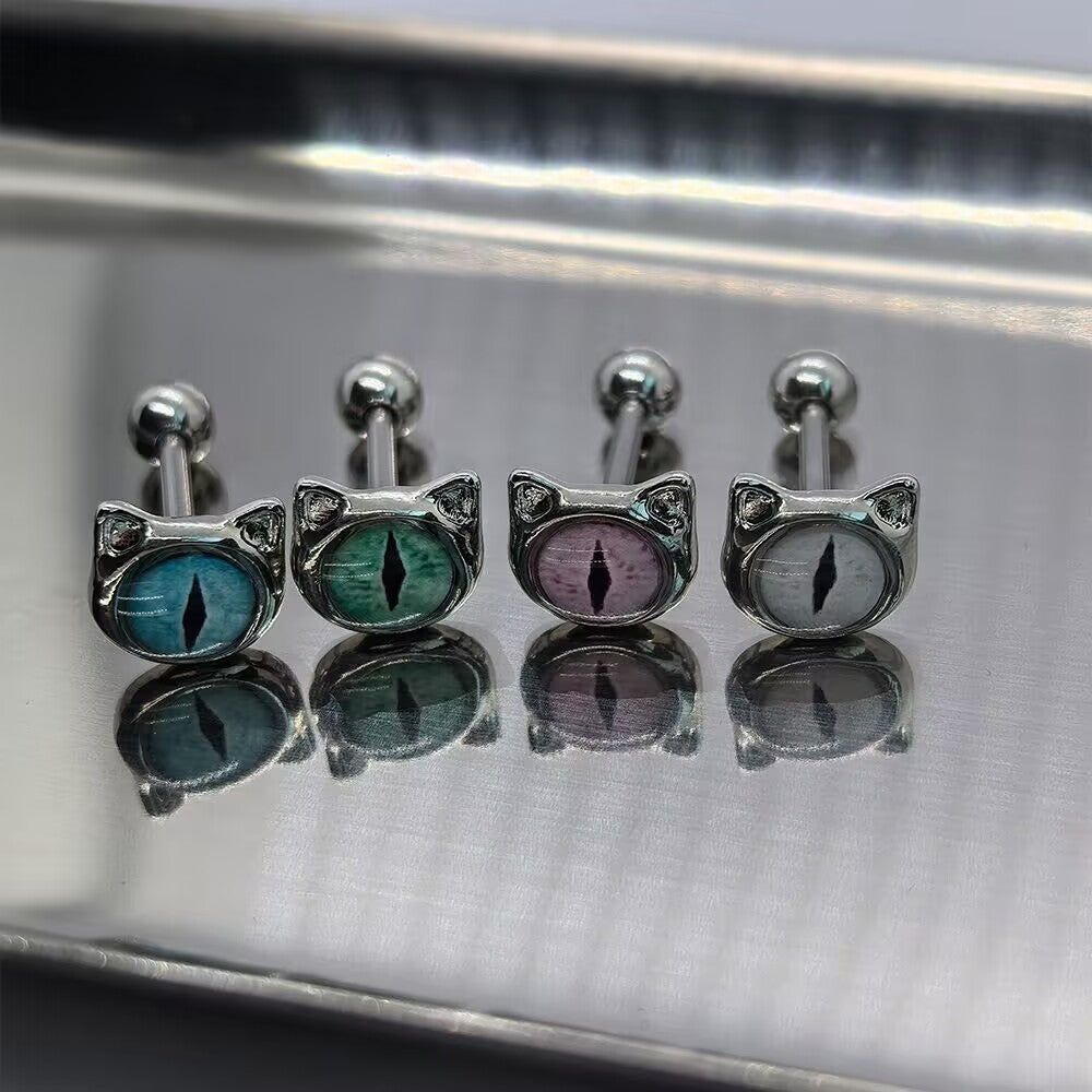Four cat eye tongue ring barbells in blue, green, purple, and gray lined up on a reflective silver tray for Gothic Y2K body piercing jewelry collection.