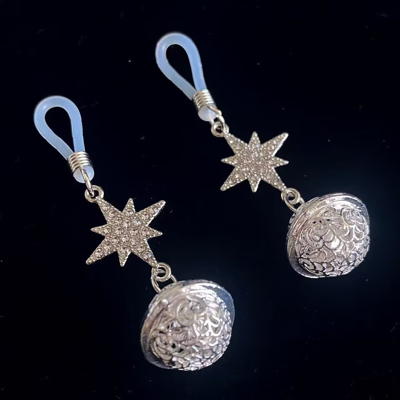 Angled close-up of shimmering star-shaped body jewelry with decorative filigree spheres on a dark background.
