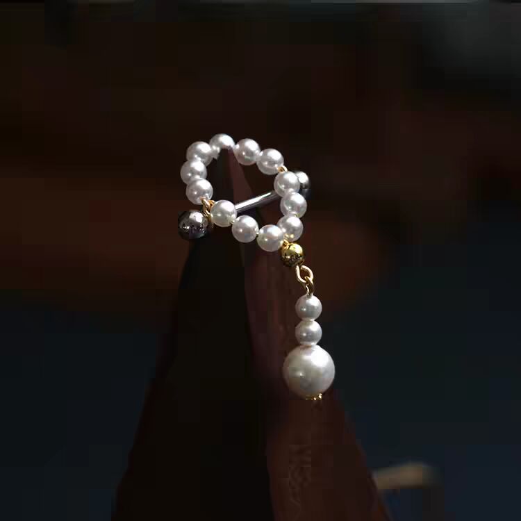 Close-up of a classic white pearl dangle nipple piercing ring with dangling pearl drop.
