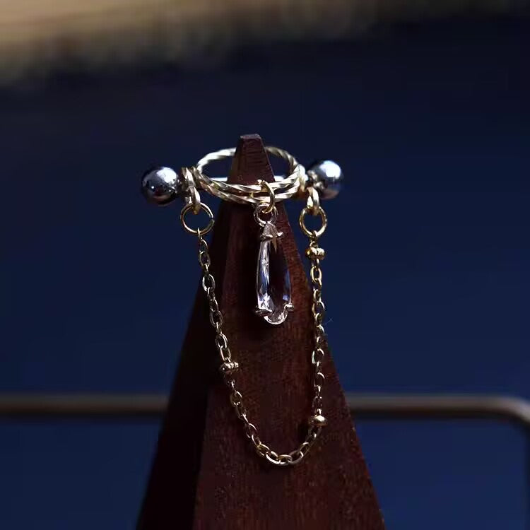 Clear white pear-cut CZ nipple shield barbell ring with delicate gold dangle chain on wooden stand display.